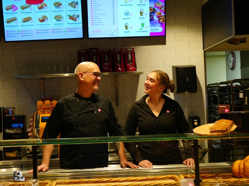 Twee mensen staan achter een toonbank en kijken naar elkaar.