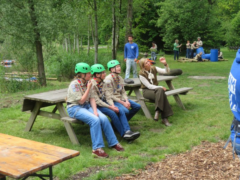 Koningin Máxima zit naast scouts op een bankje op het Scoutinglandgoed Zeewolde