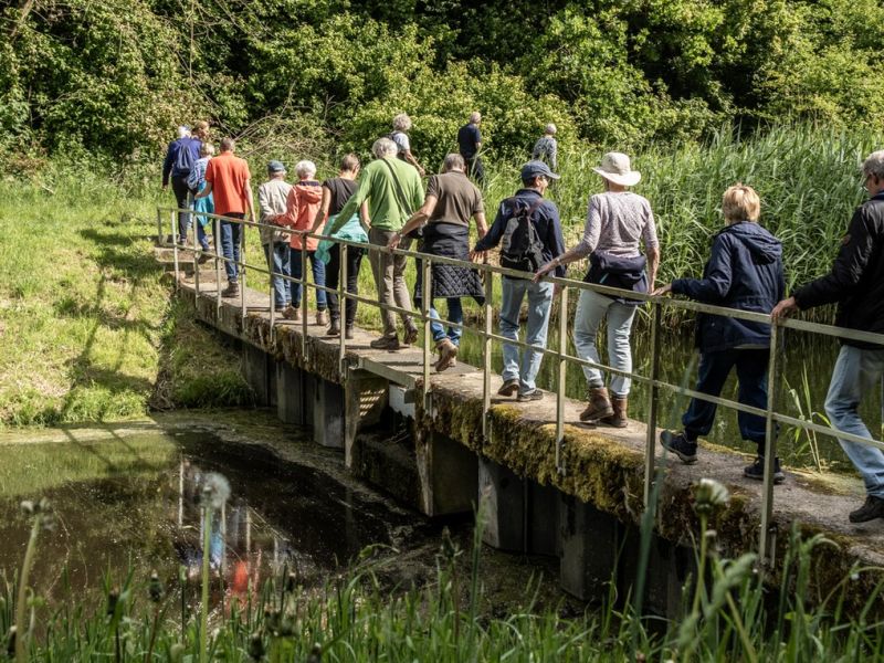 Mensen die over een dammetje wandelen naar de andere kant van de sloot