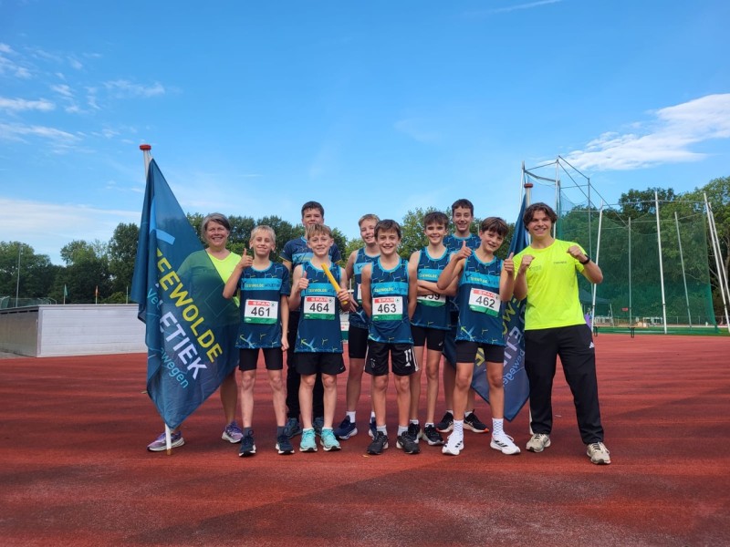 Atletiek jongens staan in sportkleding op een rij met coaches en vlag.