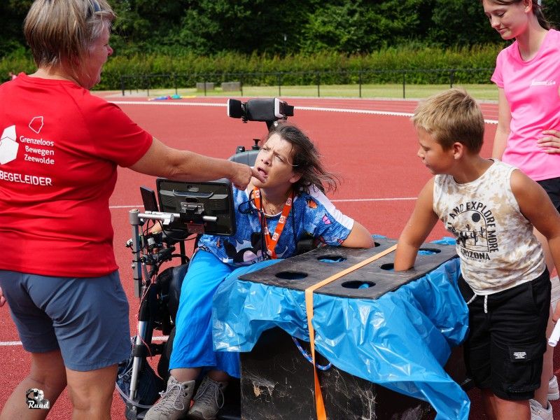 Mensen en kinderen doen onder begeleiding spelletjes op een rode atletiekbaan.