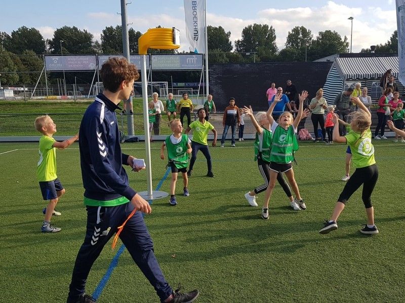 kinderen die korfballen op groen gras met gele korf.