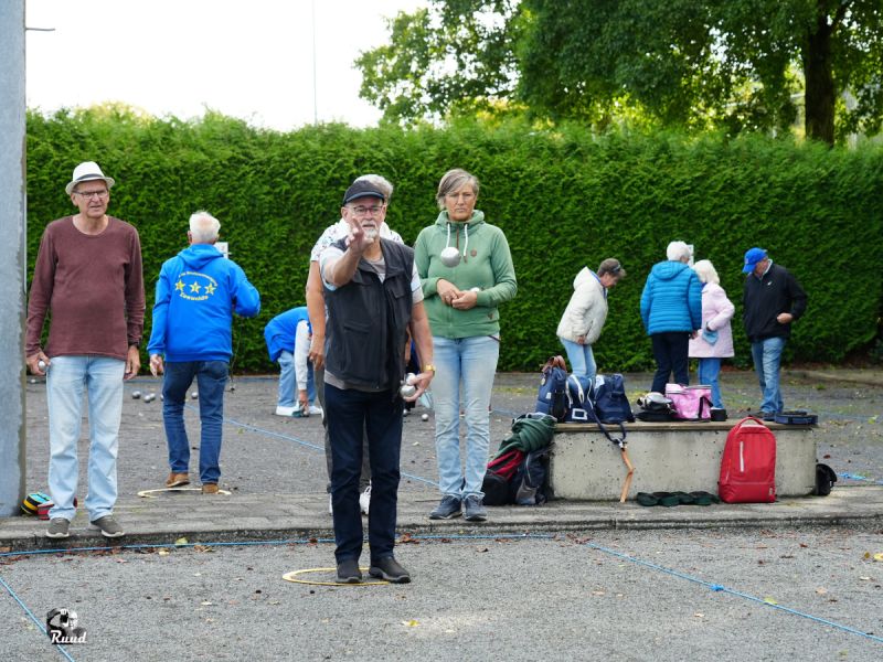Een speler die vanuit de ring de bal werpt, tegenstanders en teamlid kiken gespannen toe. Op deandere banen wordt ook druk gespeeld.