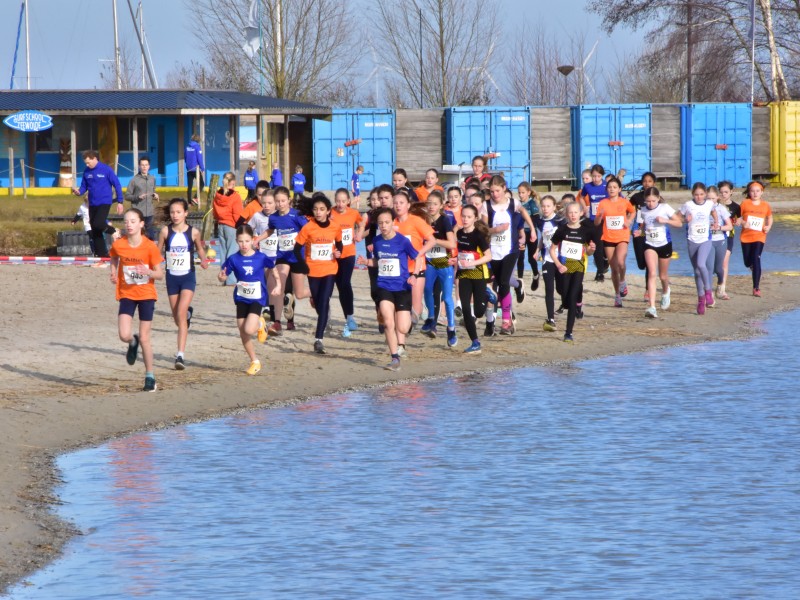 De deelnemers van de regiocross langs de waterkant van het Wolderwijd voor de surfschool langs