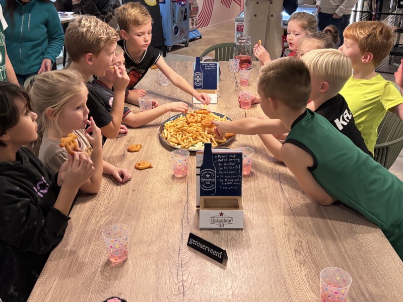 Kinderen eten patat aan een grote tafel.