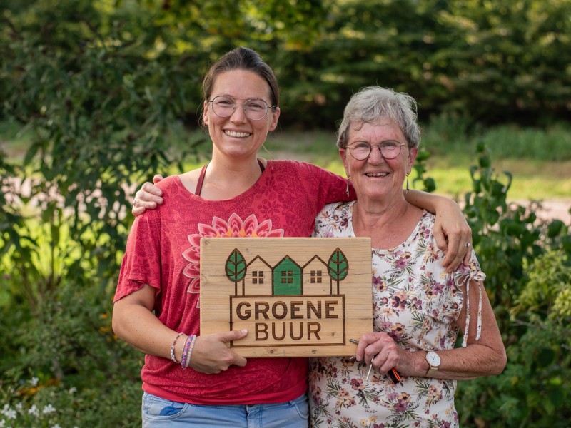 Twee mensen houden houten bordje Groene Buur vast.