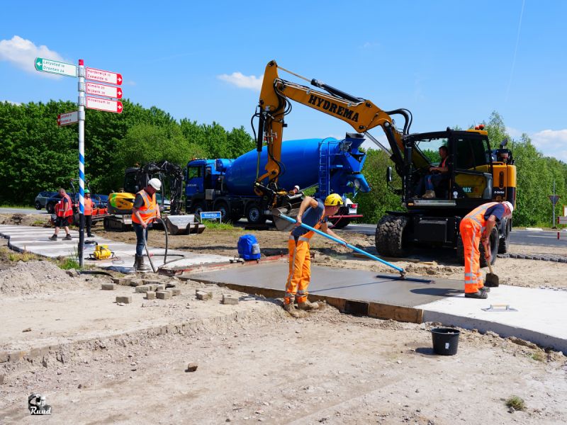 de heren aan het werk met het beton op verschillende panelen en een graafmachine en betonmolen erbij