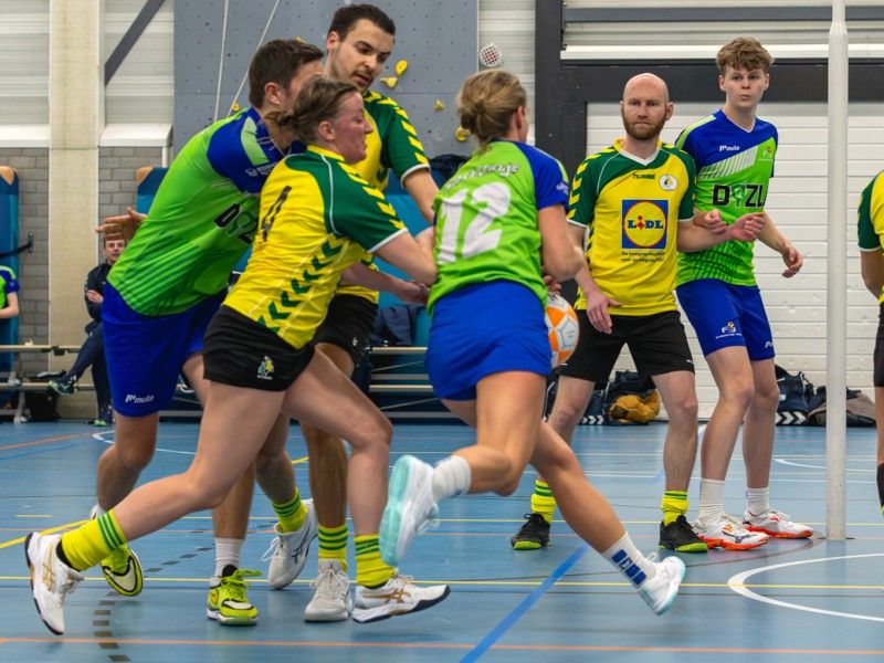 De teams strijdend om de bal in de zaal, vlak onder de korf