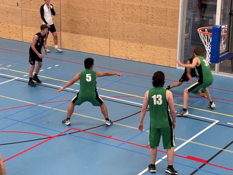 Groepje basketballers in gymzaal met blauwe vloer.