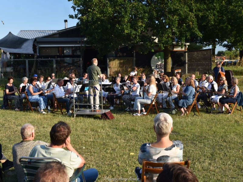 De dirigent met het orkest vlak bij Fika en publiek wat op meegebrachte stoeltjes op het gras ook zit te kijken
