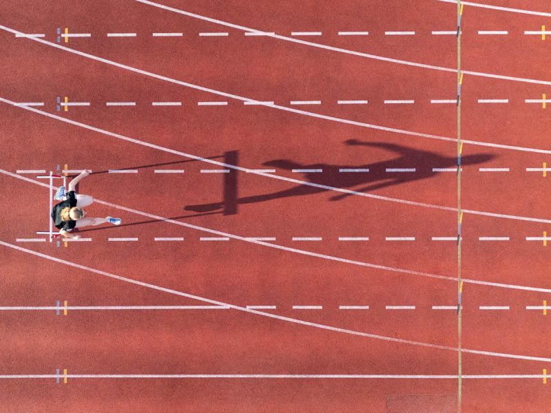 een atletiekbaan van boven een hordeloper neemt een hor op de rood oranje baan met strepen