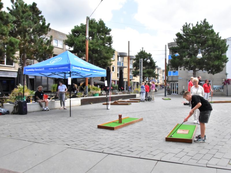 Golfbaantjes op het Kerkplein met kinderen en ouderen die er bij staan en een tent