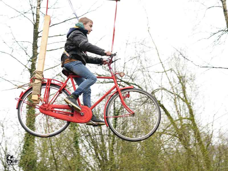 Een fiets aan een kabel in de lucht waar kinderen een oversteek mee moeten maken