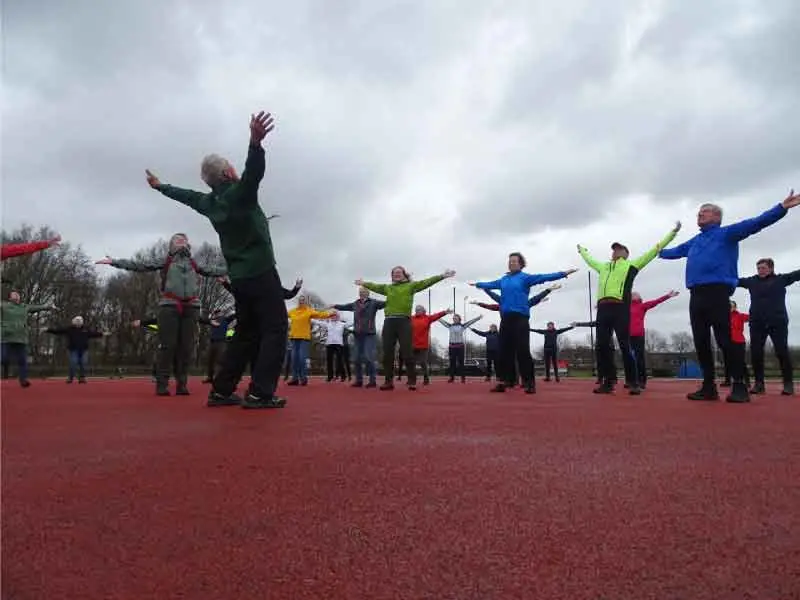 Een groep wandelaars die wat strekoefeningen doen op de atletliekbaan