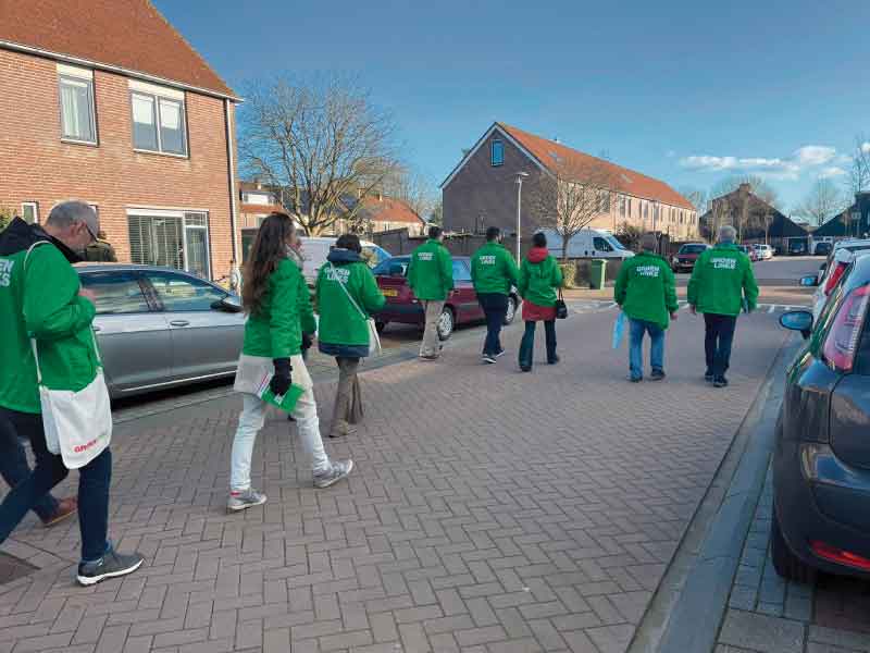 Ruim 10 campagneleden van GroenLinks in groene jassen in een straat in Zeewolde Noord