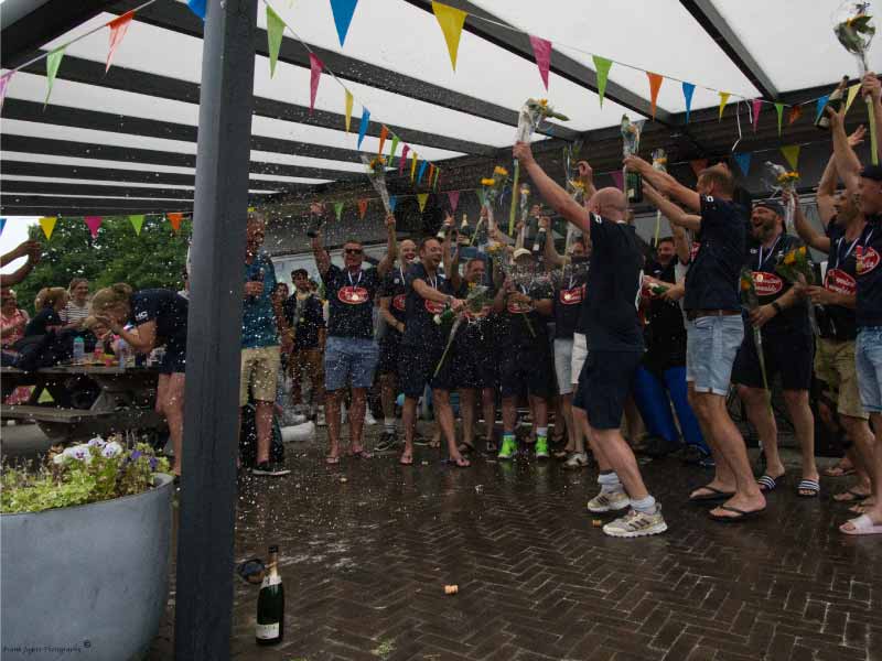 Heren veteranen vieren hun kampioenschap uitbundig met een champagne douche voor publiek