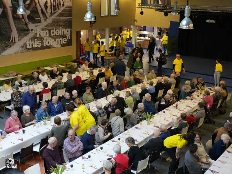 Een bovenaanzicht van lange rijen tafels in de aula van de levant waarin door lions leden en jongeren eten wordt geserveerd