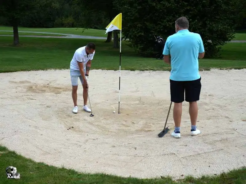 2 golfspelers die in de bunker hun bal proberen uit de holen