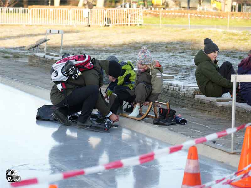 Een vader die de schaatsen om doet bij zijn kinderen aan de rand van de ijsbaan.