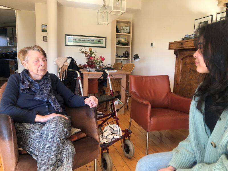Oudere mevrouw met rollator naast zich in gesprek met jongere vrouw