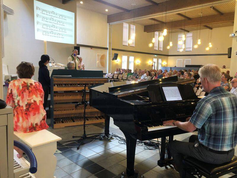 Verschillende mensen die samen muziek maken en meezingen vanaf een beamer scherm met tekst.