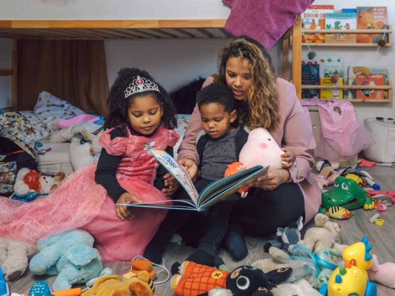 Iemand die voorleest aan 2 kinderen die bij haar zitten met allemaal knuffels eromheen