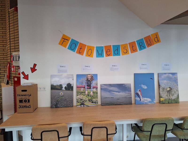 Foto's op een lange tafel met stembus er naast 