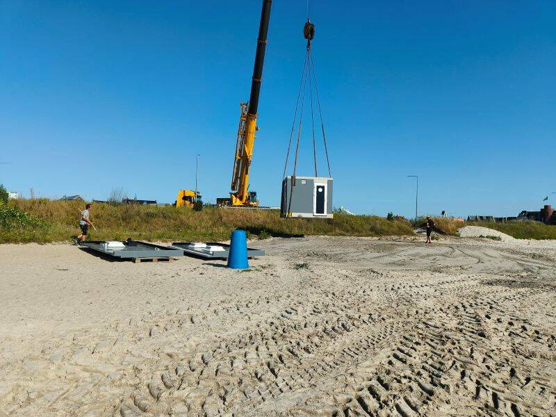strand met een gele kraan tegen een blauwe lucht die een gebouw optilt
