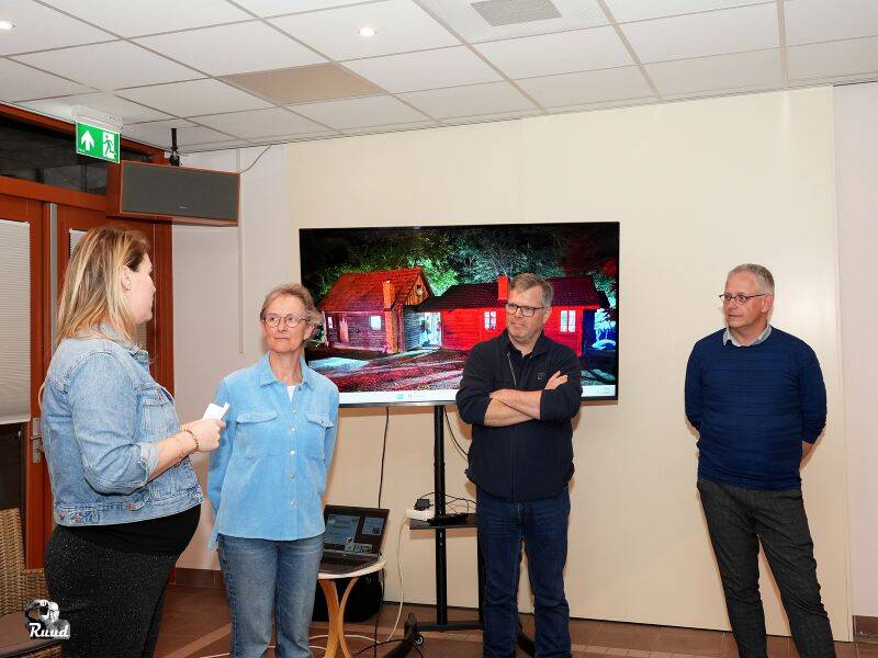 vier mensen staan voor een scherm met een foto van een huis erop