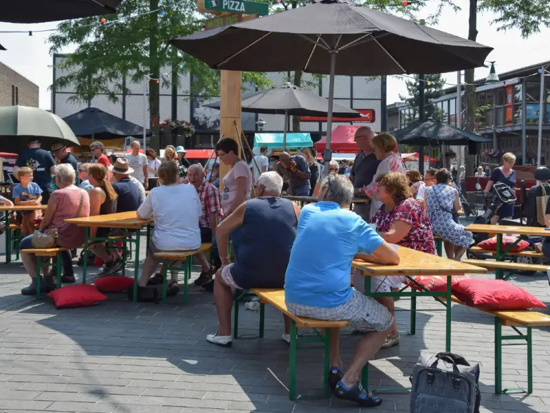 mensen op een plein zitten aan tafels met een parasol