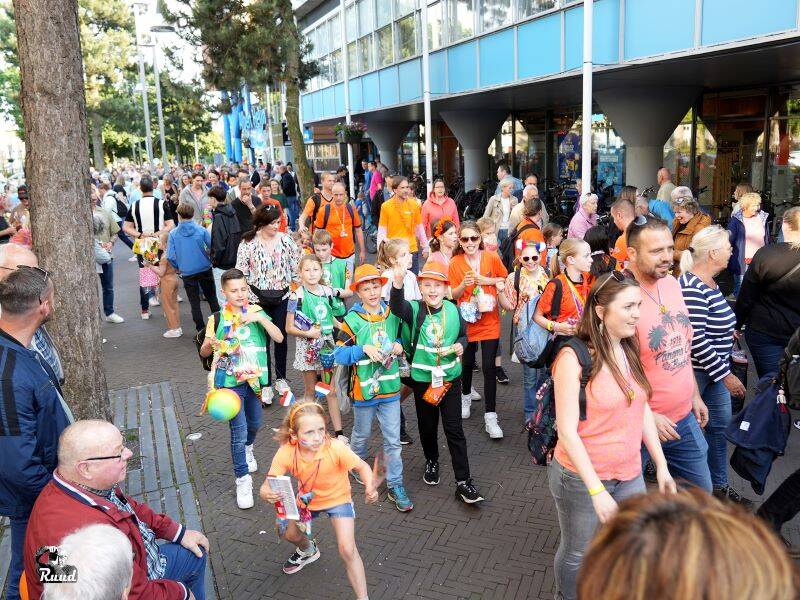 Wandelaars met verschillende kleuren t-shirts aan lopen achter elkaar in een centrum